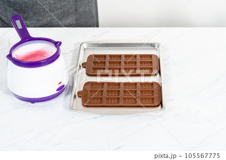 Filling silicone chocolate mold with melted chocolate to make mini pink chocolates. 105567775