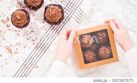 Flat lay. Step by step. Packaging chocolate cupcakes with chocolate ganache frosting into a paper cupcake box. 105567875