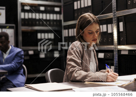 Businesswoman writing corporate report, working late at night at administrative record, analyzing bookkeeping documents in arhive room. Depository worker checking accountancy research Businesswoman writing corporate report, working late at night at administrative record, analyzing bookkeeping documents in arhive room. Depository worker checking accountancy research 105568466