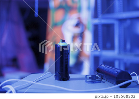Graffiti spray paint bottles in neglected urban warehouse illuminated by fluorescent blue neon lights. Containers with aerosols glowing in the dark, fluorescent lights in ghetto space. Close up. Graffiti spray paint bottles in neglected urban warehouse illuminated by fluorescent blue neon lights. Containers with aerosols glowing in the dark, fluorescent lights in ghetto space. Close up. 105568502
