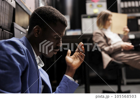 Tired diverse colleagues working overtime in arhive room, analyzing criminal case evidence. African american private detectives checking crime scene footage trying to catch mysterious suspect Tired diverse colleagues working overtime in arhive room, analyzing criminal case evidence. African american private detectives checking crime scene footage trying to catch mysterious suspect 105568503