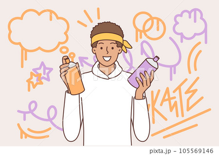Teenager guy draws graffiti on wall, holds spray can of paint and smiling looks at camera Teenager guy draws graffiti on wall, holds spray can of paint and smiling looks at camera 105569146