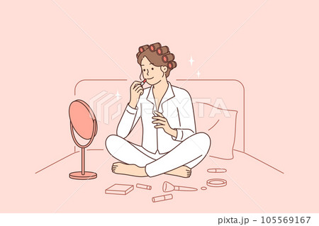 Woman does makeup while sitting in bed early in morning and paints lips while looking in mirror 105569167