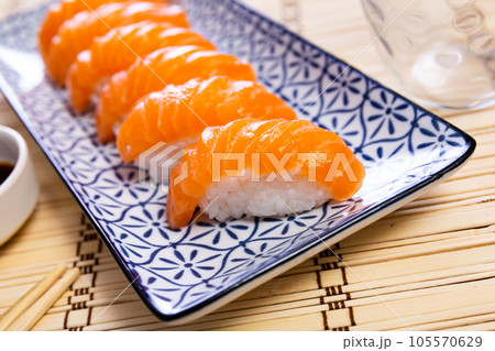 Blue rectangular ceramic plate of delicious salmon nigiri with soy souse on bamboo mat. Blue rectangular ceramic plate of delicious salmon nigiri with soy souse on bamboo mat. 105570629