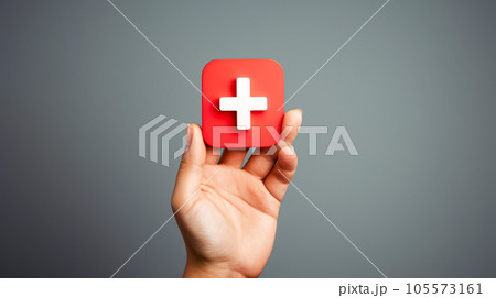 First aid concept. Hand holding a red square with a cross symbol 105573161