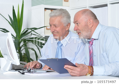 Two old business men sitting at desk and working Two old business men sitting at desk and working 105573497