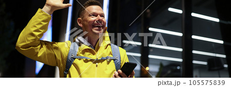 Happy man with smartphone smiles and greets friends with raised hand outdoors. Happy man with smartphone smiles and greets friends with raised hand outdoors. 105575839