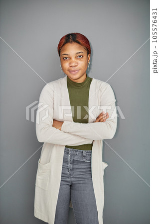 pensive dark-skinned girl standing on a gray background with her arms crossed 105576431