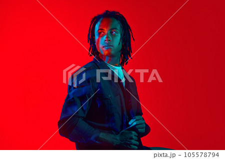 Handsome young african guy with colorful neon filter reflection on face posing against red background in neon light 105578794