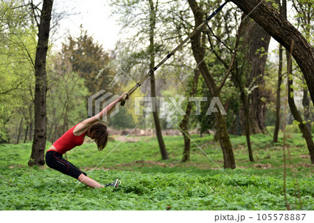 Young attractive woman does body stretching with trx fitness straps 105578887