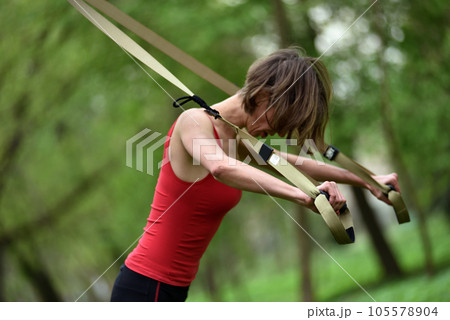 Young woman does suspension training with fitness straps in the outdoors 105578904