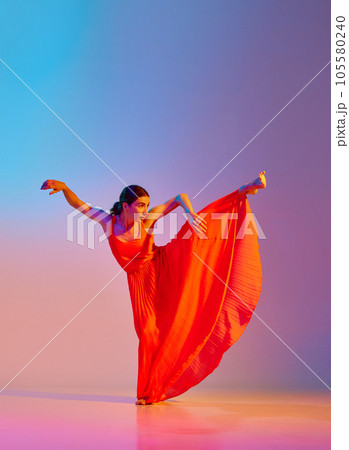 Grace and tenderness. Young beautiful woman in long elegant dress dancing against gradient multicolor background in neon light 105580240