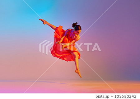 Dynamic image of artistic young woman dancing in elegant red dress against gradient multicolor background in neon light 105580242