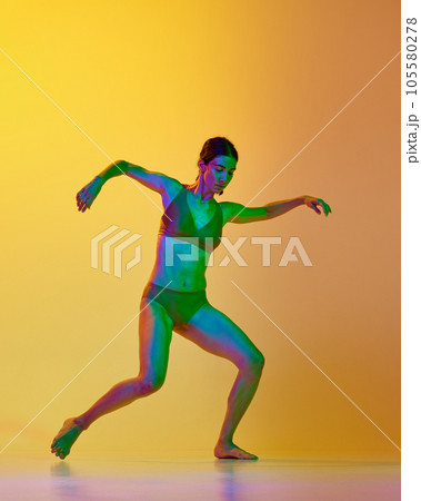 Full-length image of young woman, professional dancer in motion, dancing in underwear against gradient yellow orange background in neon light Full-length image of young woman, professional dancer in motion, dancing in underwear against gradient yellow orange background in neon light 105580278