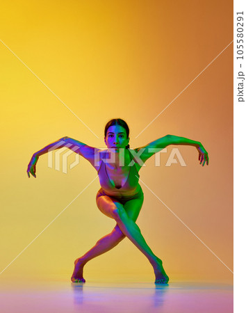Artistic, talented young woman in underwear dancing contemp against gradient yellow orange background in neon light 105580291