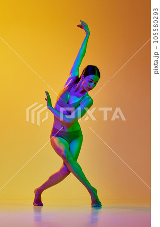 Tender young woman in underwear dancing contemp dance against gradient yellow orange background in neon light 105580293