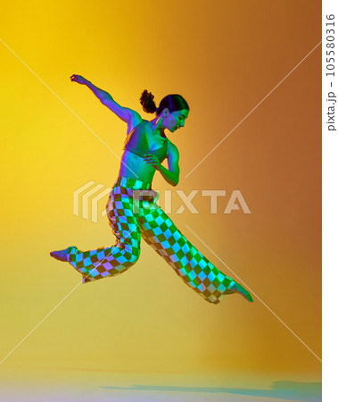 Artistic contemp performance. Young woman in stylish clothes dancing against gradient yellow orange background in neon light 105580316
