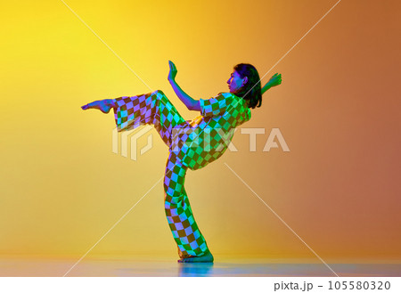 Young artistic, talented woman dancing contemporary, freestyle dance against gradient yellow orange background in neon light Young artistic, talented woman dancing contemporary, freestyle dance against gradient yellow orange background in neon light 105580320