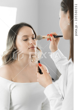 The makeup artist carefully polishes minor imperfections on a young woman's face by applying camouflage that helps create the perfect makeup canvas. 105580351