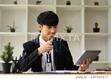 Male economist drinking coffee and using digital tablet, working with sales statistics document at office desk. 105582677