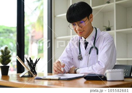 Portrait of general practitioner in white uniform sitting in modern workplace and filling medical form. Portrait of general practitioner in white uniform sitting in modern workplace and filling medical form. 105582681