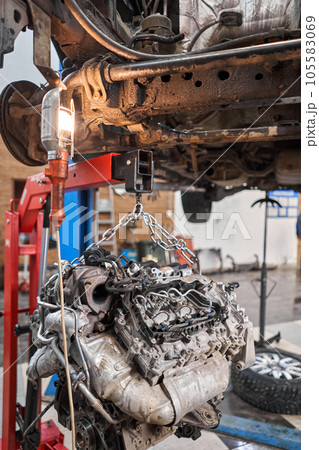 A car mechanic inspects the engine with a flashlight. Engine Block on a repair stand with Special crane jack. Technical service station for car. 105583069