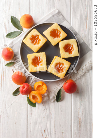 Square soft cookies with apricot jam close-up on a plate. Vertical top view 105585653