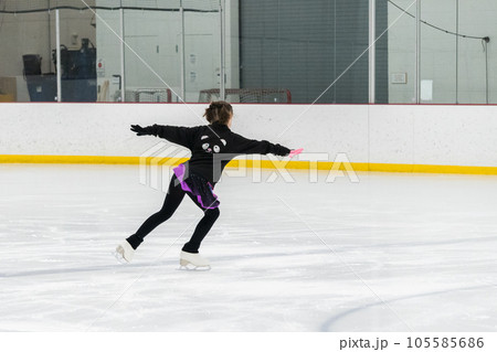 Young girl perfecting her figure skating routine while wearing her competition dress at an indoor ice rink. 105585686