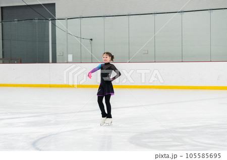 Young girl perfecting her figure skating routine while wearing her competition dress at an indoor ice rink. Young girl perfecting her figure skating routine while wearing her competition dress at an indoor ice rink. 105585695