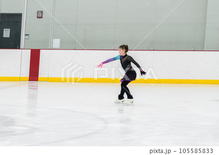 Young girl perfecting her figure skating routine while wearing her competition dress at an indoor ice rink. 105585833