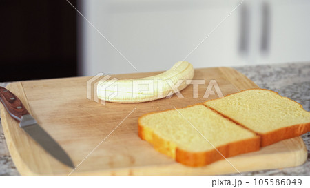 In a modern white kitchen, buttered banana and brioche bread are being prepared for making a delicious grilled peanut butter banana sandwich. In a modern white kitchen, buttered banana and brioche bread are being prepared for making a delicious grilled peanut butter banana sandwich. 105586049