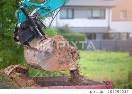 A bucket of excavator pours the ground into a heap against the background of a rural industrial zone. Bulldozer work on the construction site. A bucket of excavator pours the ground into a heap against the background of a rural industrial zone. Bulldozer work on the construction site. 105590587