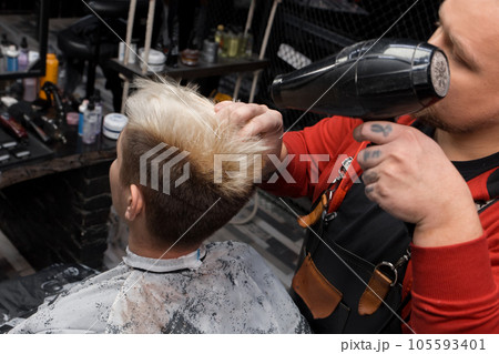 The hands of a male barber salon worker blow dry a client's hair before a haircut at work The hands of a male barber salon worker blow dry a client's hair before a haircut at work 105593401