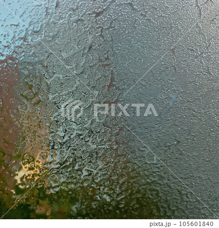 Frozen glass with the onset of cold weather. View through a layer of ice to the blue sky. Frost on the windshield, the rays of the morning sun melt the frost formed overnight. Background, texture. 105601840
