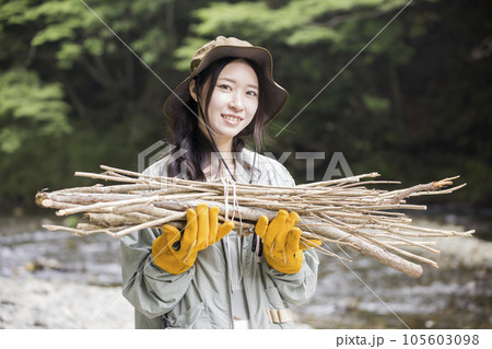 キャンプ場で焚き火用の枝を拾ってくる若い女性 105603098