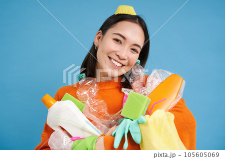 Portrait of smiling korean girl, holding sorted garbage for recycling, looks happy, cares for nature and environment, blue background Portrait of smiling korean girl, holding sorted garbage for recycling, looks happy, cares for nature and environment, blue background 105605069