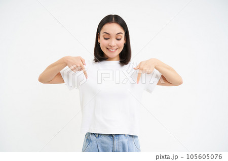 Portrait of beautiful smiling korean girl, points fingers down, shows advertisement, demonstrates banner below, isolated on white background 105605076