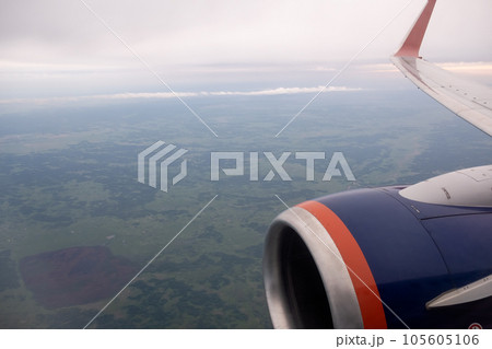 Airplane flight. Wing of an airplane flying above the clouds. View from the window of the plane. Airplane, Aircraft. Traveling by air. Aircraft's wing and land seen through the illuminator. Airplane flight. Wing of an airplane flying above the clouds. View from the window of the plane. Airplane, Aircraft. Traveling by air. Aircraft's wing and land seen through the illuminator. 105605106
