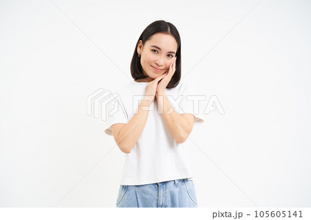 Portrait of tender, cute young asian woman, looking with flirty, silly ace expression, standing over white background 105605141
