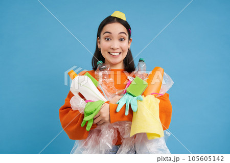 Girl with different types of plastic waste, trash in her hands, smiling and looking enthusiastic, recycle her garbage, blue background 105605142