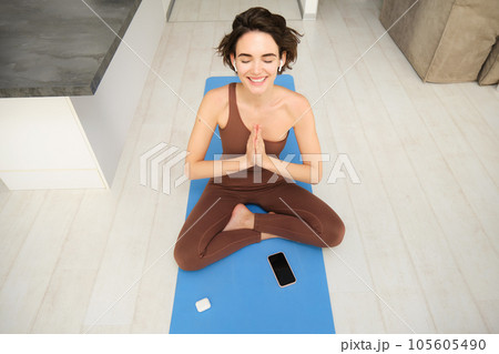 Top view young sporty slim woman meditating, asana lotus posture relax, breathing with happy smile, sitting on rubber yoga mat 105605490