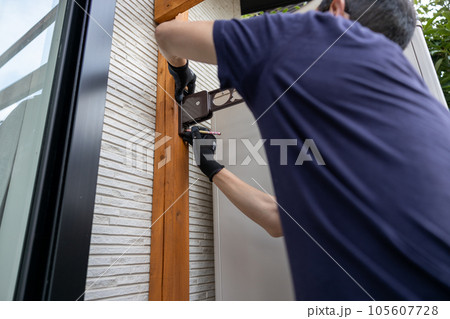 工具を使って木の柱に物干し用金具をつけているところ 105607728