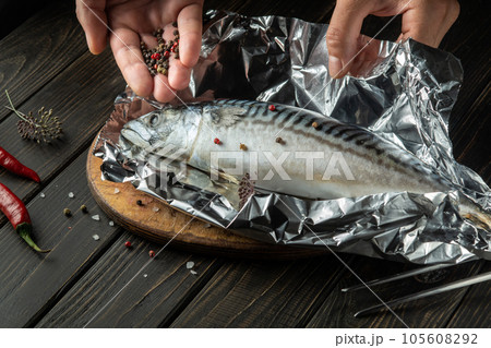 The chef adds fragrant spices and pepper to mackerel fish before preparing a delicious lunch on the kitchen table 105608292