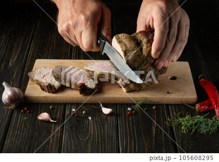 The chef cuts the grilled veal meat into small slices. Work environment on the kitchen table with condiments or spices. Black background with space for recipe or menu. The chef cuts the grilled veal meat into small slices. Work environment on the kitchen table with condiments or spices. Black background with space for recipe or menu. 105608295
