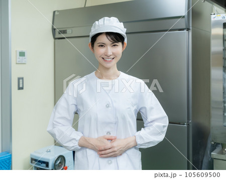 調理室の中に立つ調理服を着た若い女性 105609500