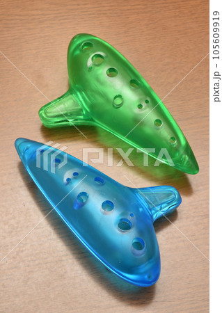 プラスチックで作られた青と緑の半透明色でカラフルな子供用のオカリナ、木の背景 プラスチックで作られた青と緑の半透明色でカラフルな子供用のオカリナ、木の背景 105609919