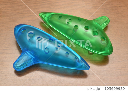 プラスチックで作られた青と緑の半透明色でカラフルな子供用のオカリナ、木の背景 プラスチックで作られた青と緑の半透明色でカラフルな子供用のオカリナ、木の背景 105609920