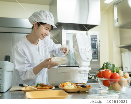 調理室で炊飯器からご飯をよそう調理服を着た若い女性 調理室で炊飯器からご飯をよそう調理服を着た若い女性 105610021