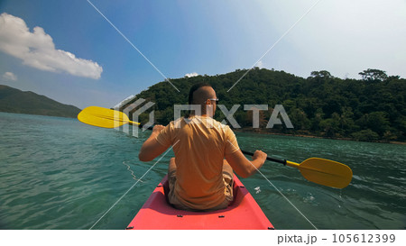 Man with sunglasses and hat rows pink plastic canoe along sea ag Man with sunglasses and hat rows pink plastic canoe along sea ag 105612399