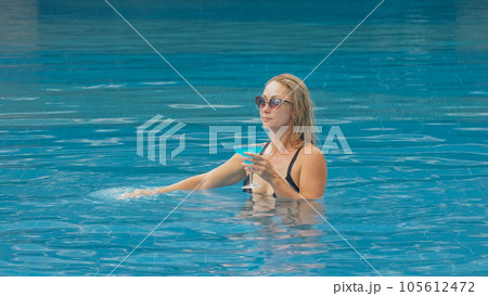 The wide middle shot pretty woman drinking blue cocktail alcohol liquor in swimming pool at hotel. Portrait of sexy girl in pool outdoor. The wide middle shot pretty woman drinking blue cocktail alcohol liquor in swimming pool at hotel. Portrait of sexy girl in pool outdoor. 105612472